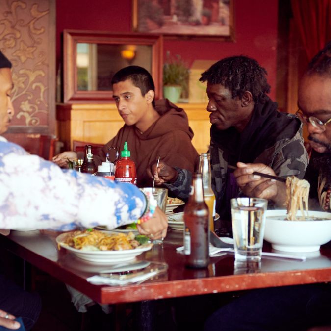 Four men eat Vietnamese food at a wooden table