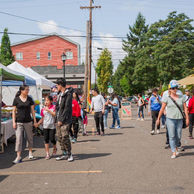 Patrons of all ages shop at a famrers market in an urban parking lot