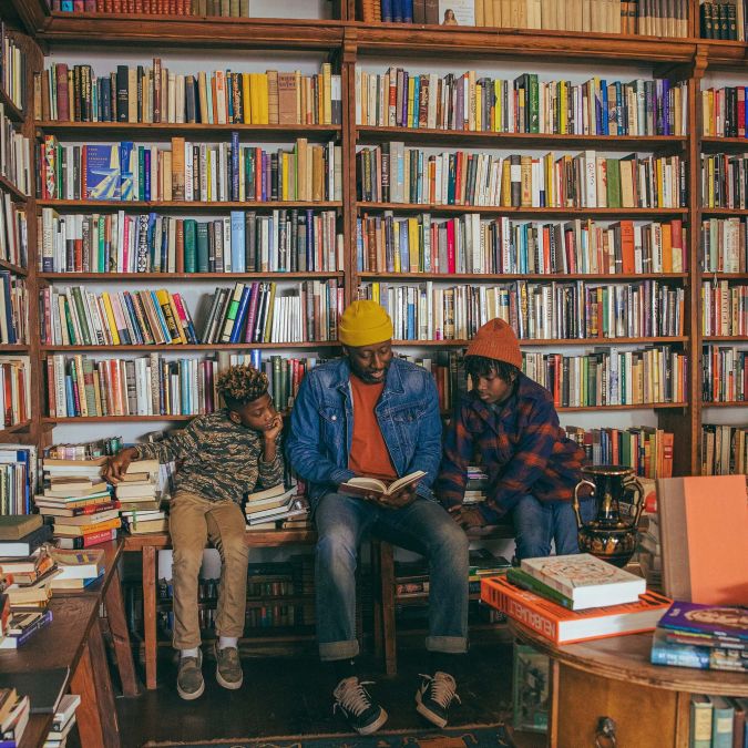 Three people sit and read a book at Mother Foucault's bookstore in front of a wall of books.