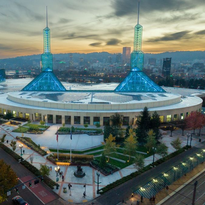 a vast building with two spires at sunset with the city skyline and hills in the background