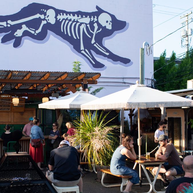 people dining outside at benches under a mural