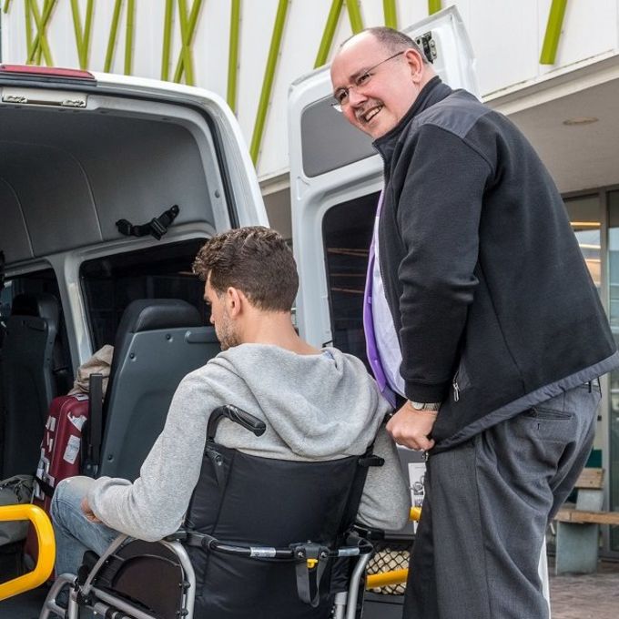 One man helps another man in a wheelchair into a van