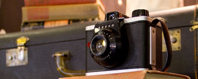 a vintage camera and suitcase displayed along with old hardcover books