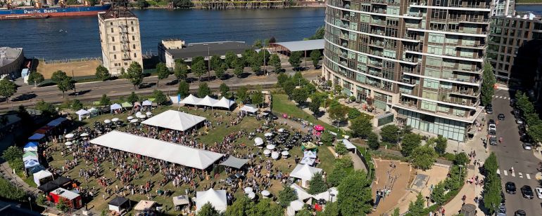 Aerial shot of an urban riverside park with festival tents and umbrellas