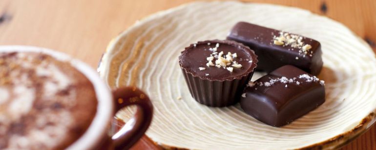 dish of truffle chocolates next to a mug of coffee on a wooden coffee table