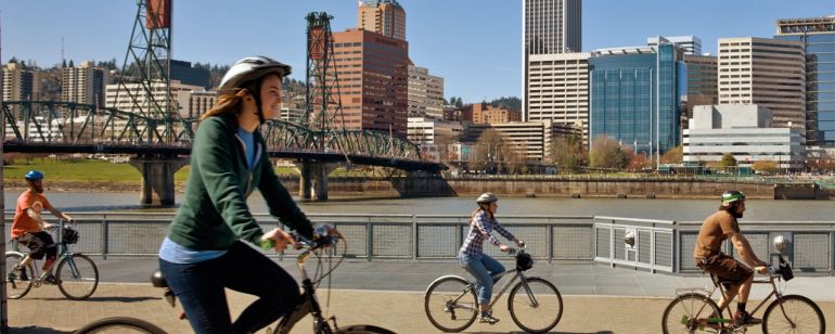bikers riding along the east bank of the Willamette river with the Hawthorne bridge and Portland downtown buildings in background