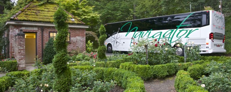 a large white motorcoach parked amid lush gardens in Washington Park
