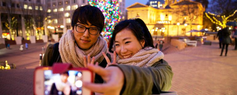 two people taking a selfie in front of portland\'s christmas tree