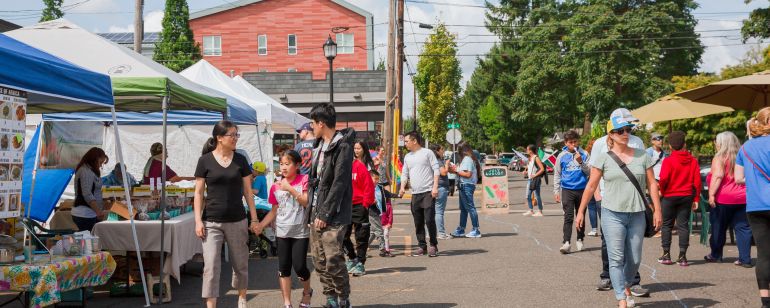 Patrons of all ages shop at a famrers market in an urban parking lot