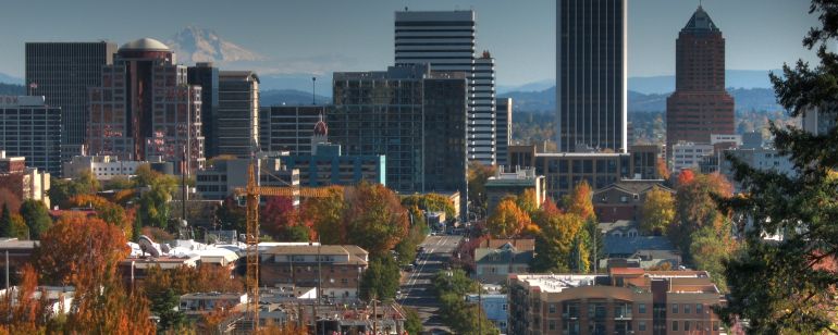 A view of city skyline with its trees a fiery autumn orange with a snow-capped mountain in the background.