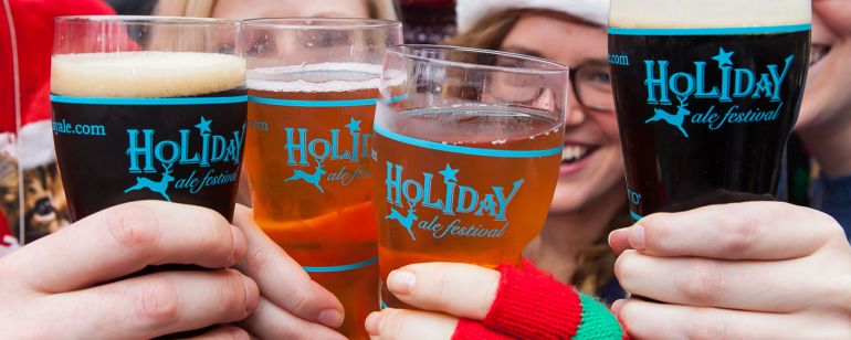 four beer drinkers wearing hats and gloves clink glasses