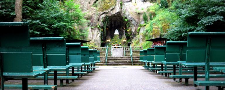 rows of benches face a rock wall and tunnel surrounded by moss, trees