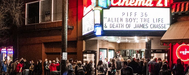 A crowd of move goers gather beneath the Cinema 21 marquee at night