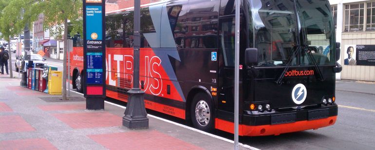 The red and black bolt bus waits curbside for passengers