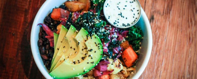 a bowl of brightly colored vegetables with avocado slices on top and a dressing on the side