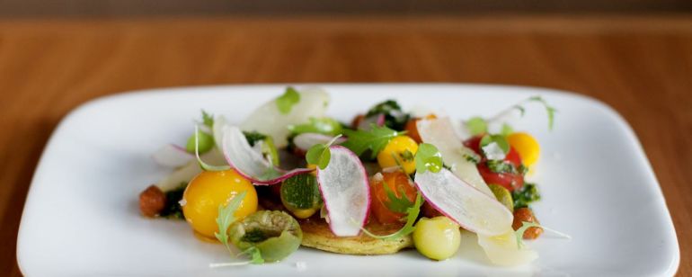 a white platter of delicately prepared, colorful vegetables on a wooden table