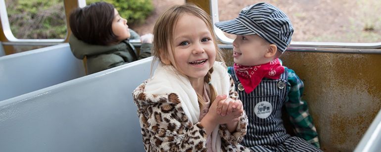 two children sitting on a train, one is dressed like a train conductor