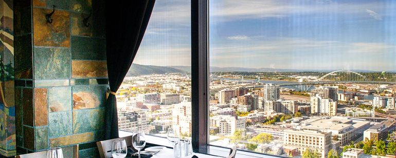 A table set with a white tablecloth next to a window with a scenic city view