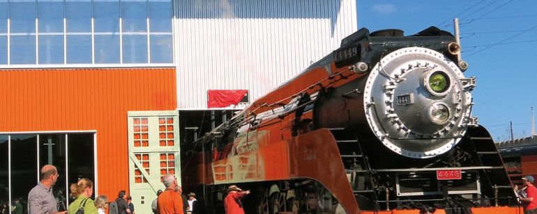 Many people are admiring a bright orange steam engine at the Oregon Rail Heritage Center.