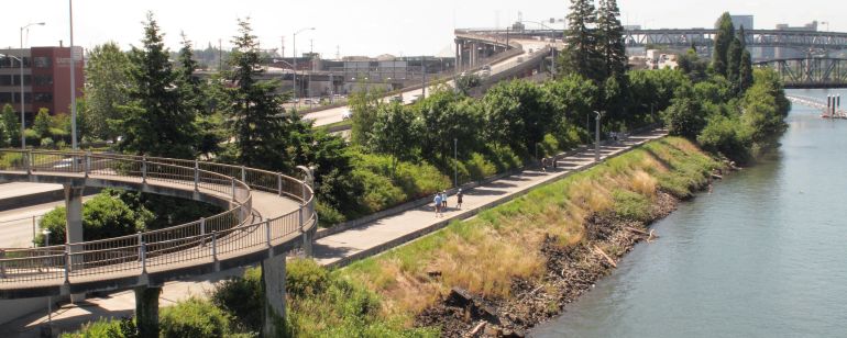 Three people use a riverside path flanked by a highway