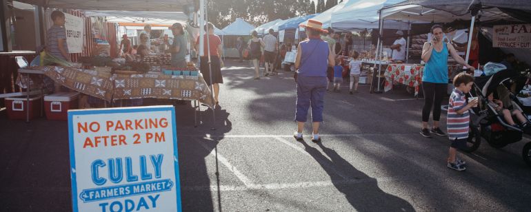 a parking lot filled with farmers market vendors, and a sign for the cully farmers market