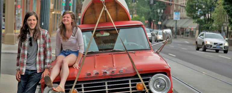 two people next to an orange truck with a canoe strapped to the top