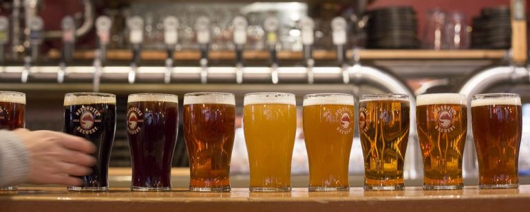 7 pints of beer lined up from dark to light