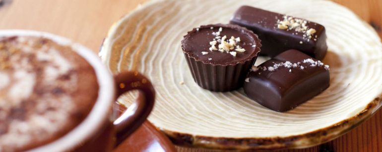 dish of truffle chocolates next to a mug of coffee on a wooden coffee table