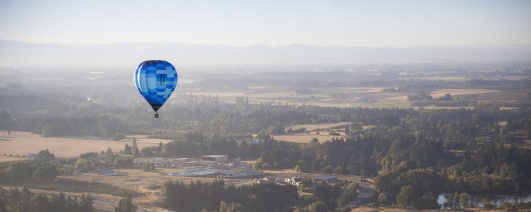 A hot air balloon floats above a wooded valley.