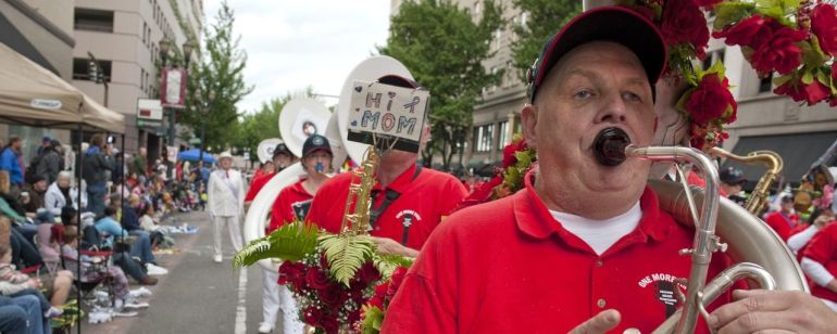 A tuba player wearing a red shirt, marching with a band in a parade