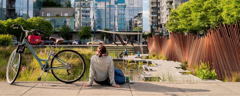 woman sitting on the ground in front of a pondwith a bicycle next to her