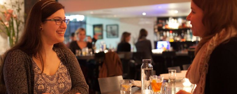 two women talking over cocktails in a warmly lit restaurant