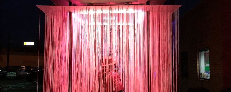 a person walks through a light installation containing long strands of lights hanging from a panel overhead