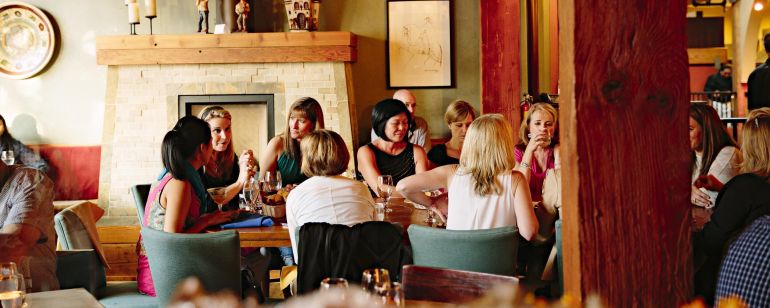 a group of people enjoy drinks and conversation around a large table in a warmly lit restaurant