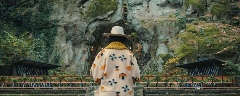 A person stands with their back facing the camera in front of a natural stone wall