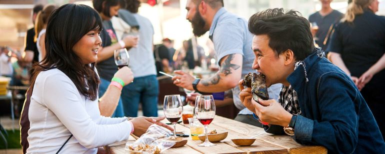 two people eating food and drinking wine at a picnic table