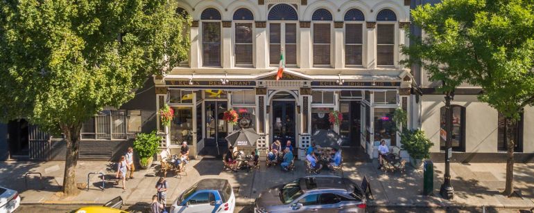 the facade of a large Irish pub with groups of people eating and drinking out front