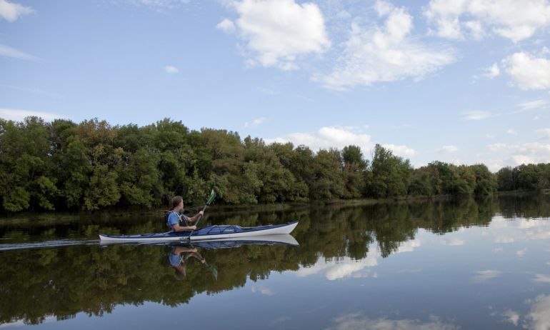 a person kayaking on glassy water with puffy clouds reflected in it