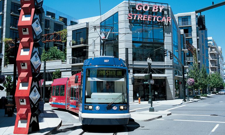 A streetcar passes by a large, red sculpture in front of a building with a neon sign reading, \"Go By Streetcar.\"