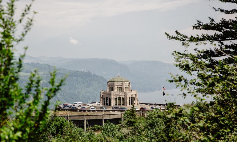 the vista house is in the distance, framed by brush and tree branches on three sides in the foreground