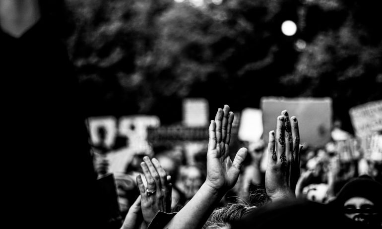 black and white image of hands raised within a crowd of protesters