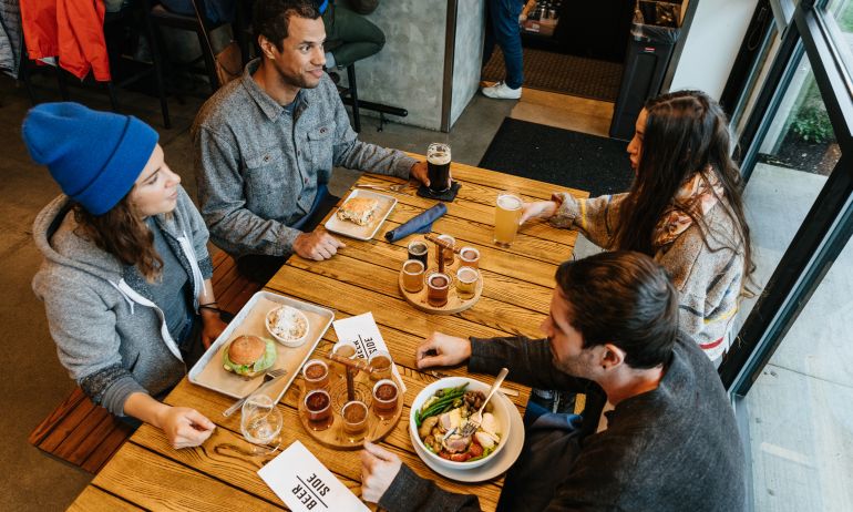 a group of four around a wooden table enjoy draft beers and pub food