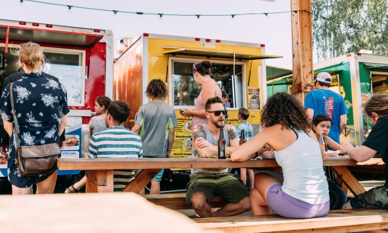 people sit at picnic tables in front of food carts