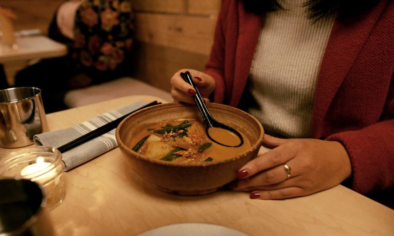 A person sitting at a table holds a ramen spoon in a bowl