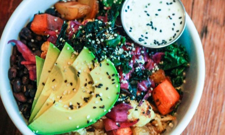 a bowl of brightly colored vegetables with avocado slices on top and a dressing on the side