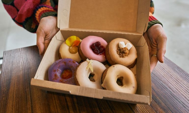 six doughnuts in a box with toppings such as marshmallows, raspberries and flower petals