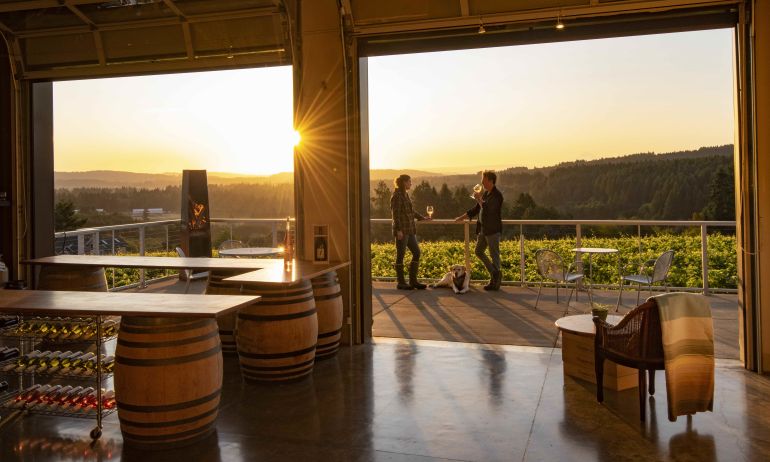 people stand on a patio sipping wine with a view of the valley as the sun sets