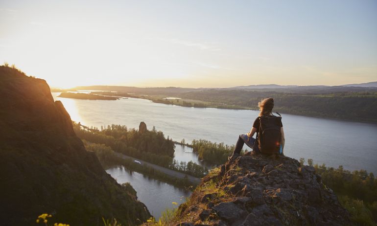 person sits on top of a rock overlooking the Columbia River as the sun sets
