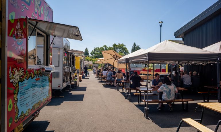 a row of food carts and diners enjoying covered outdoor seating on a sunny day