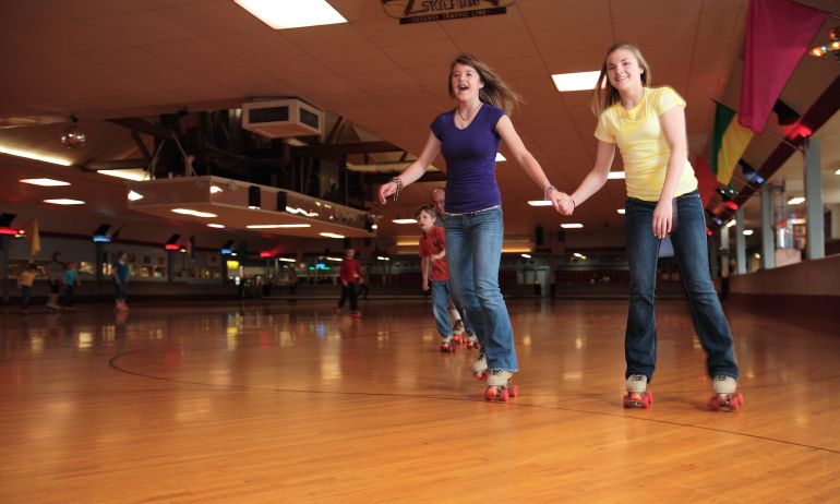 two people smile while holding hands and skating across a classic wooden roller rink